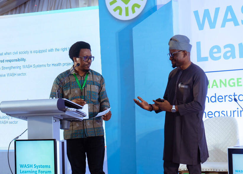 Two persons on stage at the WASH Systems for Health Nigeria Learning Forum