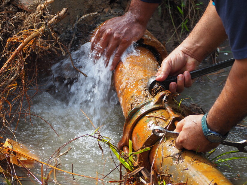 Men fixing a leaking drinking water pipe (photo by Adobe)