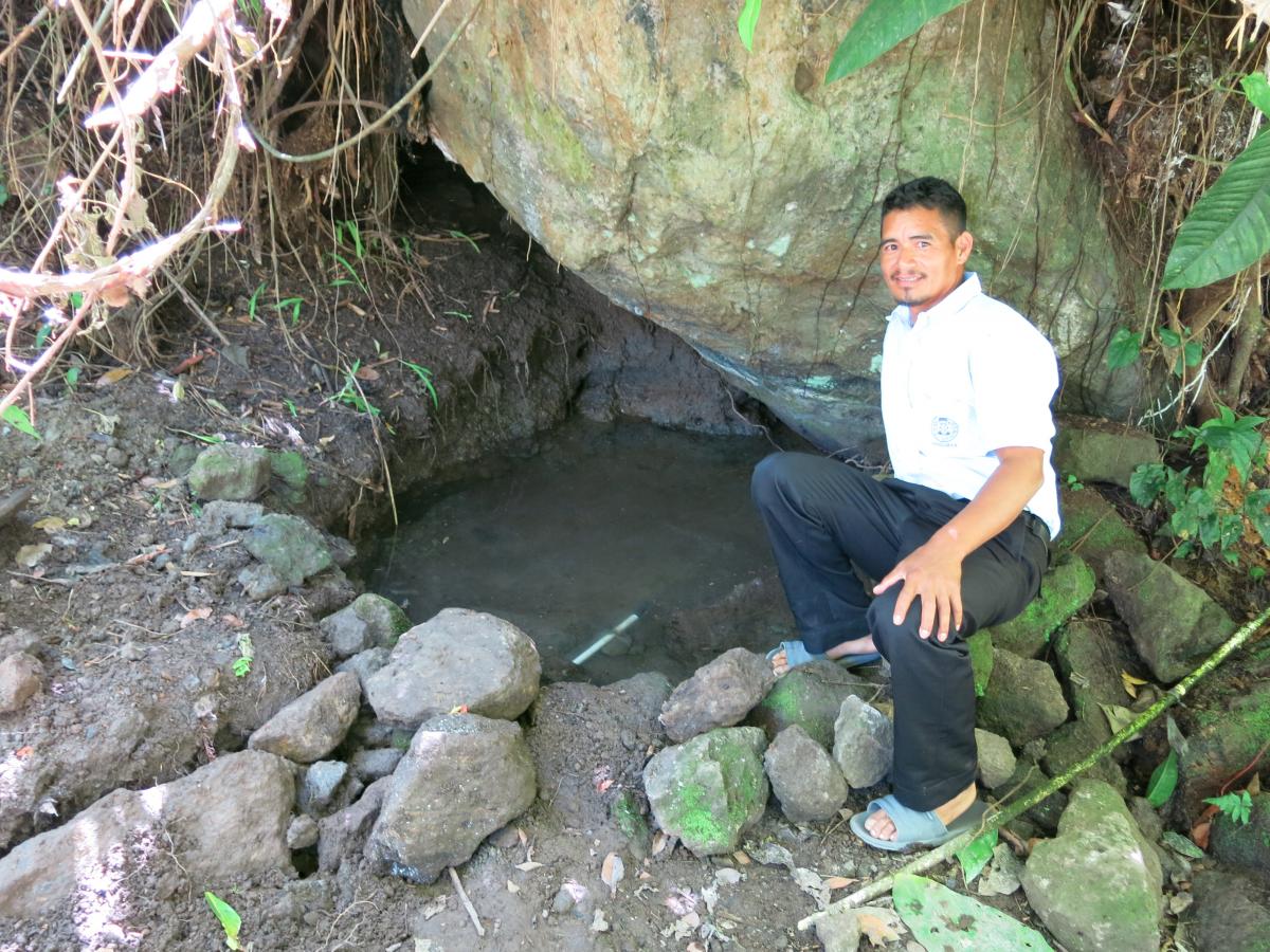 Mr. Enoc showing the spring and the tube that carries the water to his house
