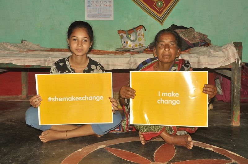 Young woman holding "#shemakeschange" card sitting next to old woman holding "#I make change", Odisha, India