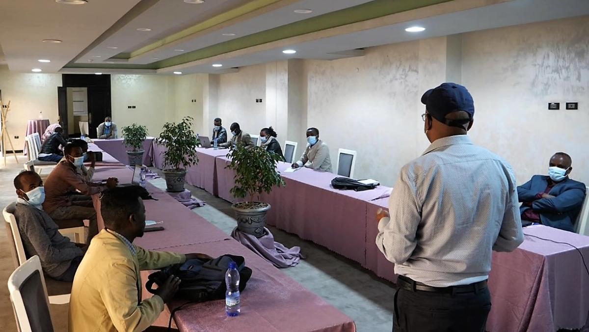 Speaker in front of room facing two rows of people with back to camera